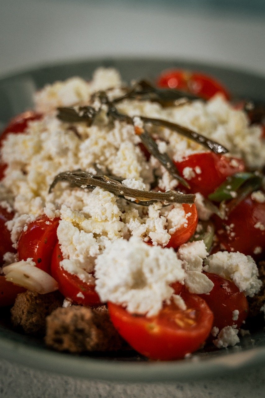Salade met cherrytomaten, feta kaas, gedroogde tomaat en kruiden in een kom.